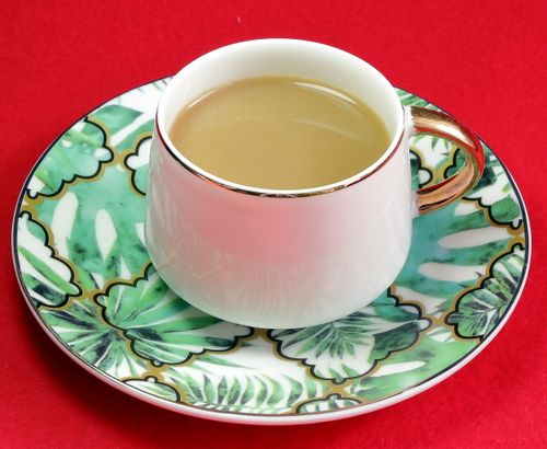 Free A stylish tea cup with a golden handle placed on a leaf-patterned saucer against a red background. Stock Photo