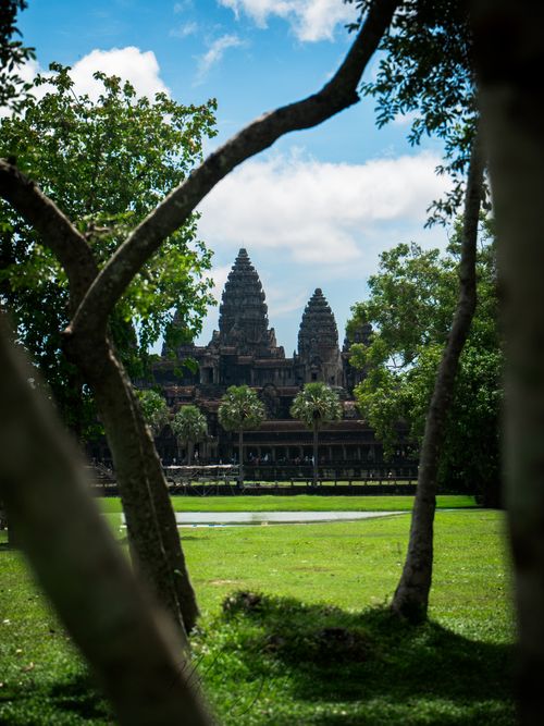 Free Scenic view of Angkor Wat temple framed by lush trees at daytime in Cambodia. Stock Photo