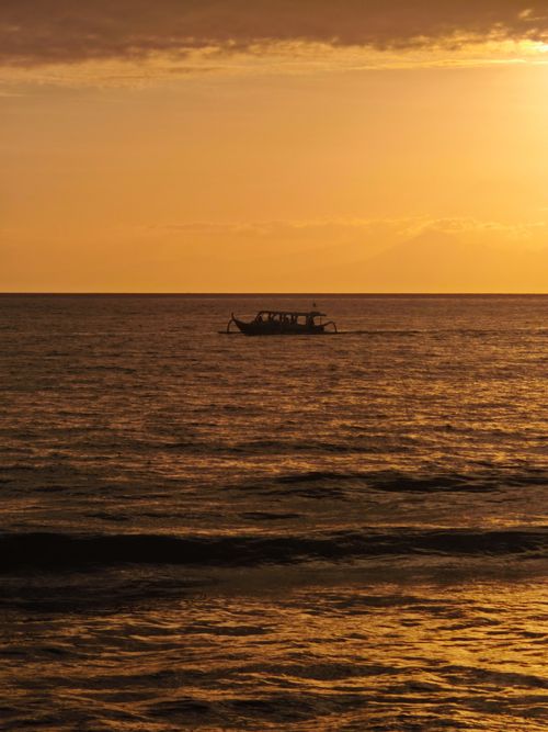Free A solitary boat floats on the tranquil ocean during a stunning golden sunset, casting a peaceful ambiance. Stock Photo