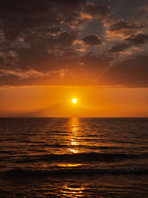 Free Captivating sunset over the ocean, casting warm orange hues with dramatic clouds. Stock Photo