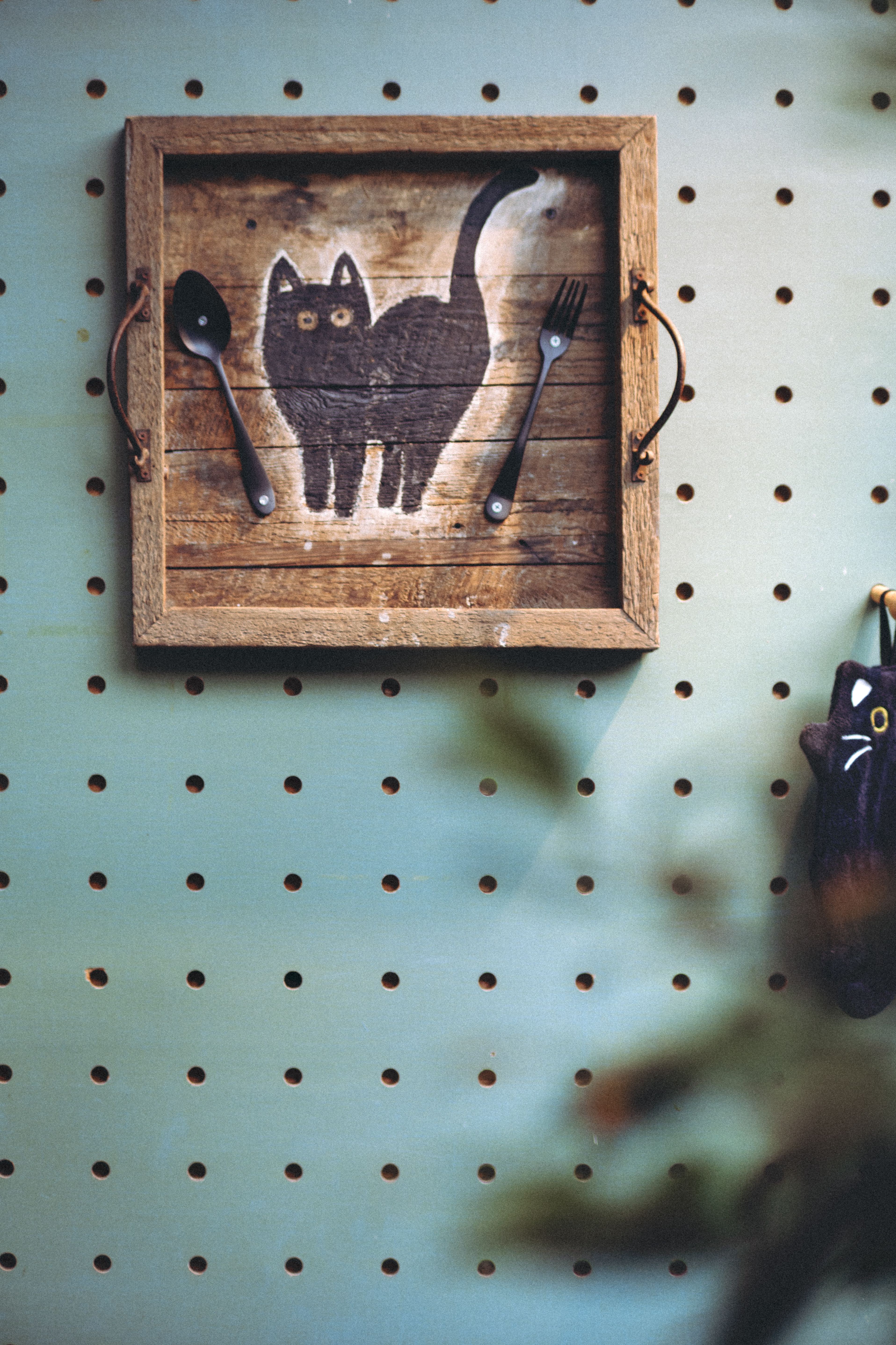 Wall art with a cat design, spoon, and fork decor on a wooden pegboard.