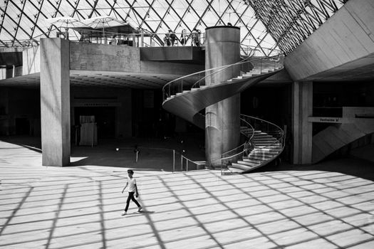 A striking black and white shot highlighting the spiral staircase and glass pyramid of the Louvre Museum.