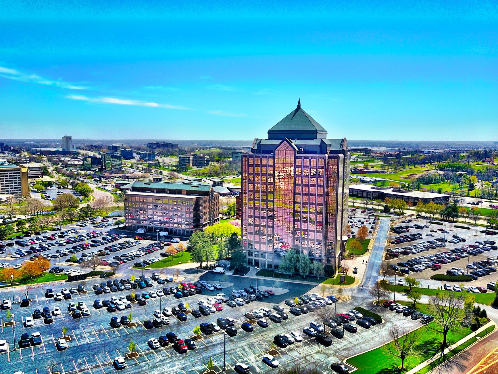 Bird's-eye view of a modern skyscraper and parking lot in Overland Park, KS, under a clear blue sky.