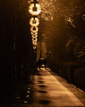 Silhouetted pedestrians walk along a sunlit Berlin street at dawn near Brandenburg Gate.