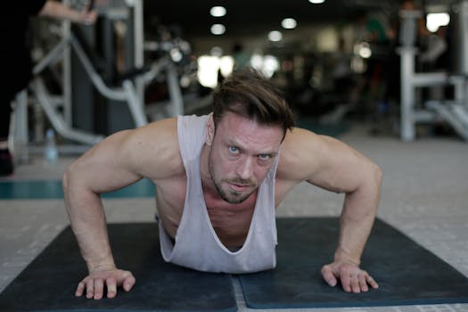 Determined adult muscular male athlete wearing sportswear performing handstand push up exercise during fitness workout on floor of modern spacious sport club and looking at camera