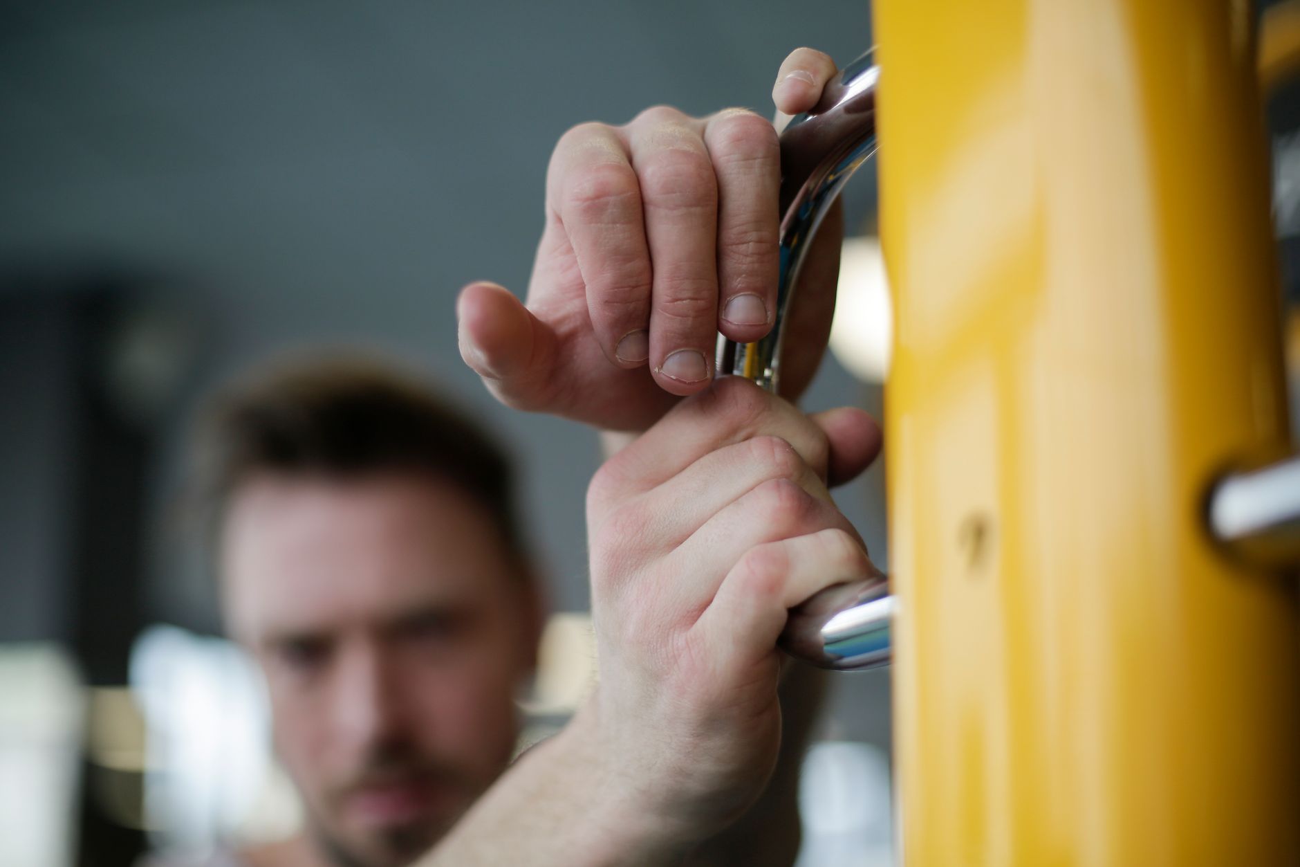 Closeup young male athlete standing with hands on yellow parallel bar during sport training on blurred background of modern fitness center