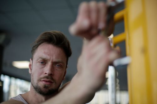 Free Determined bearded male athlete standing with hands on parallel bar during sport training on blurred background of modern fitness center and looking at camera Stock Photo