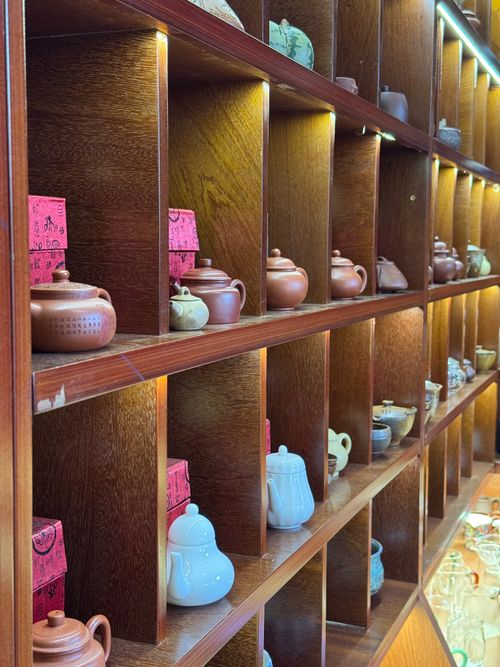 Free A variety of teapots displayed on wooden shelves in warm lighting, capturing a traditional aesthetic. Stock Photo