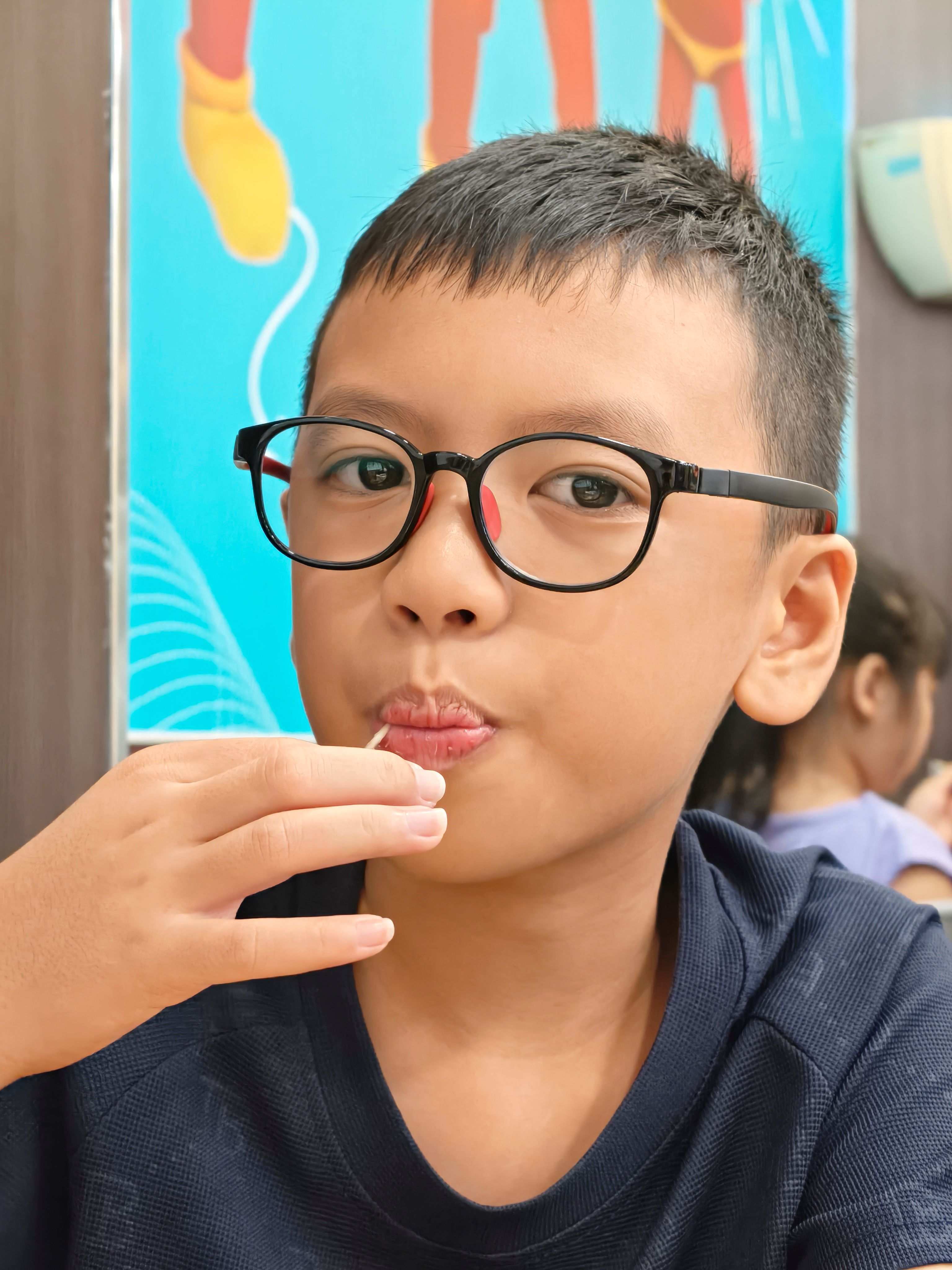 A young boy wearing glasses enjoys a sweet treat inside a colorful setting.