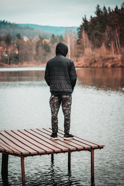 Free Man in Black Jacket Standing on Brown Wooden Dock Stock Photo