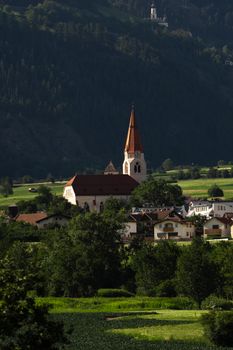 Charming village view featuring a church and lush green mountains in a serene valley setting.