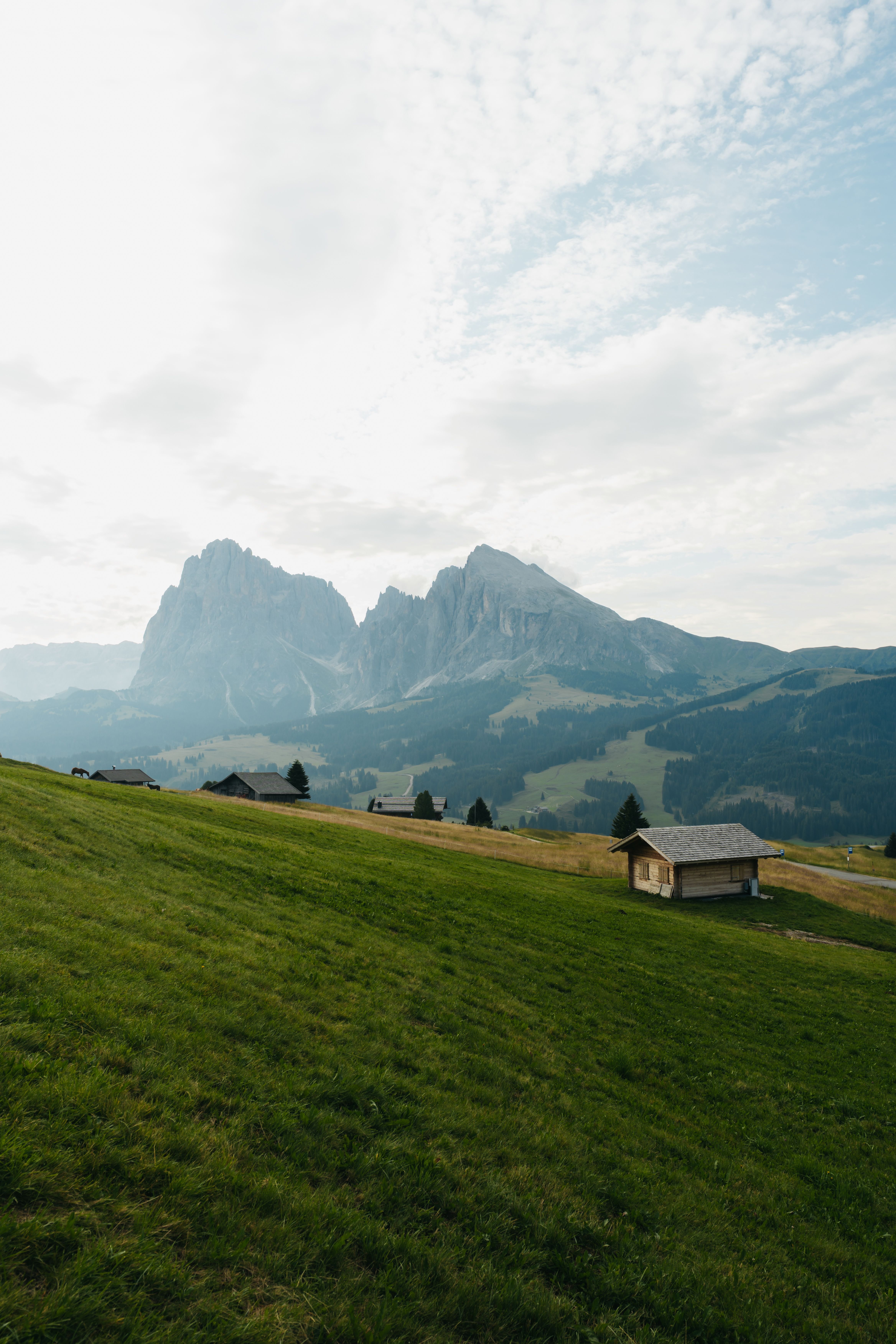 Peaceful alpine scenery featuring wooden cabins and majestic mountains under a cloudy sky.
