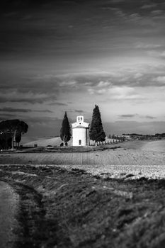 Black and white photo of a serene chapel framed by cypress trees in the rolling hills of Tuscany.
