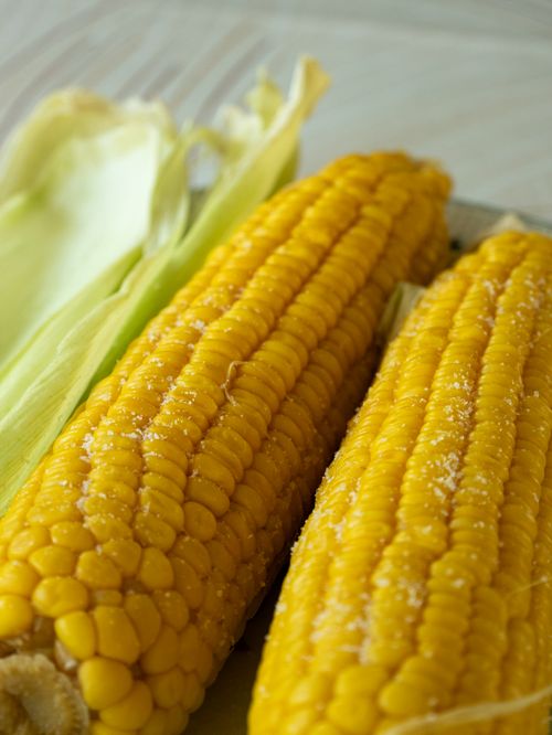 Free Delicious close-up of two corn on the cob ears with butter and salt, ideal for food and summer themes. Stock Photo