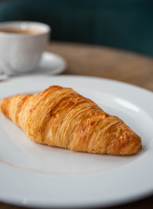 Free A freshly baked croissant served on a white plate with a cup of coffee in a cozy café. Stock Photo