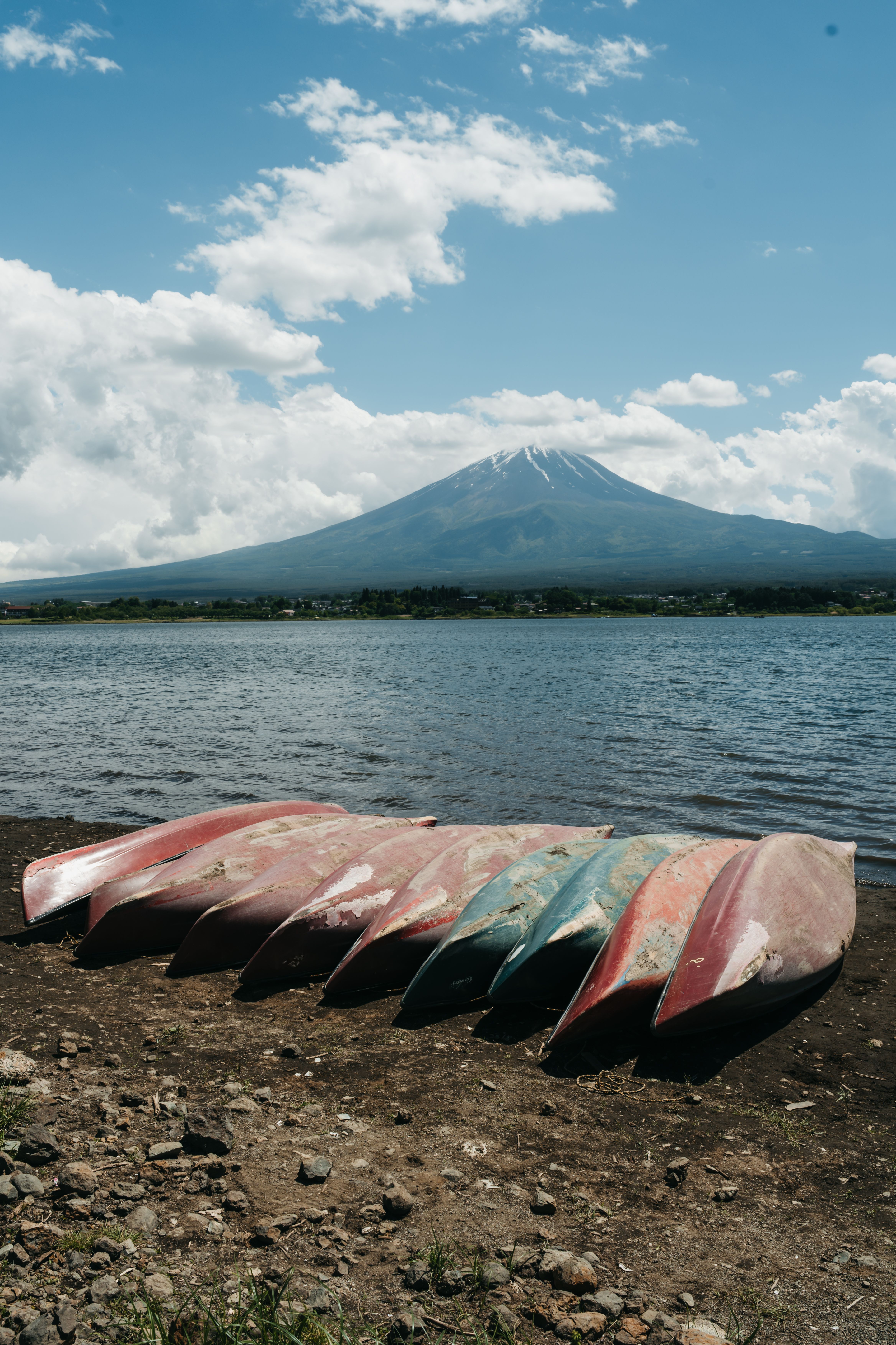 Canoes on a lakeside with Mount Fuji in the background under blue skies.