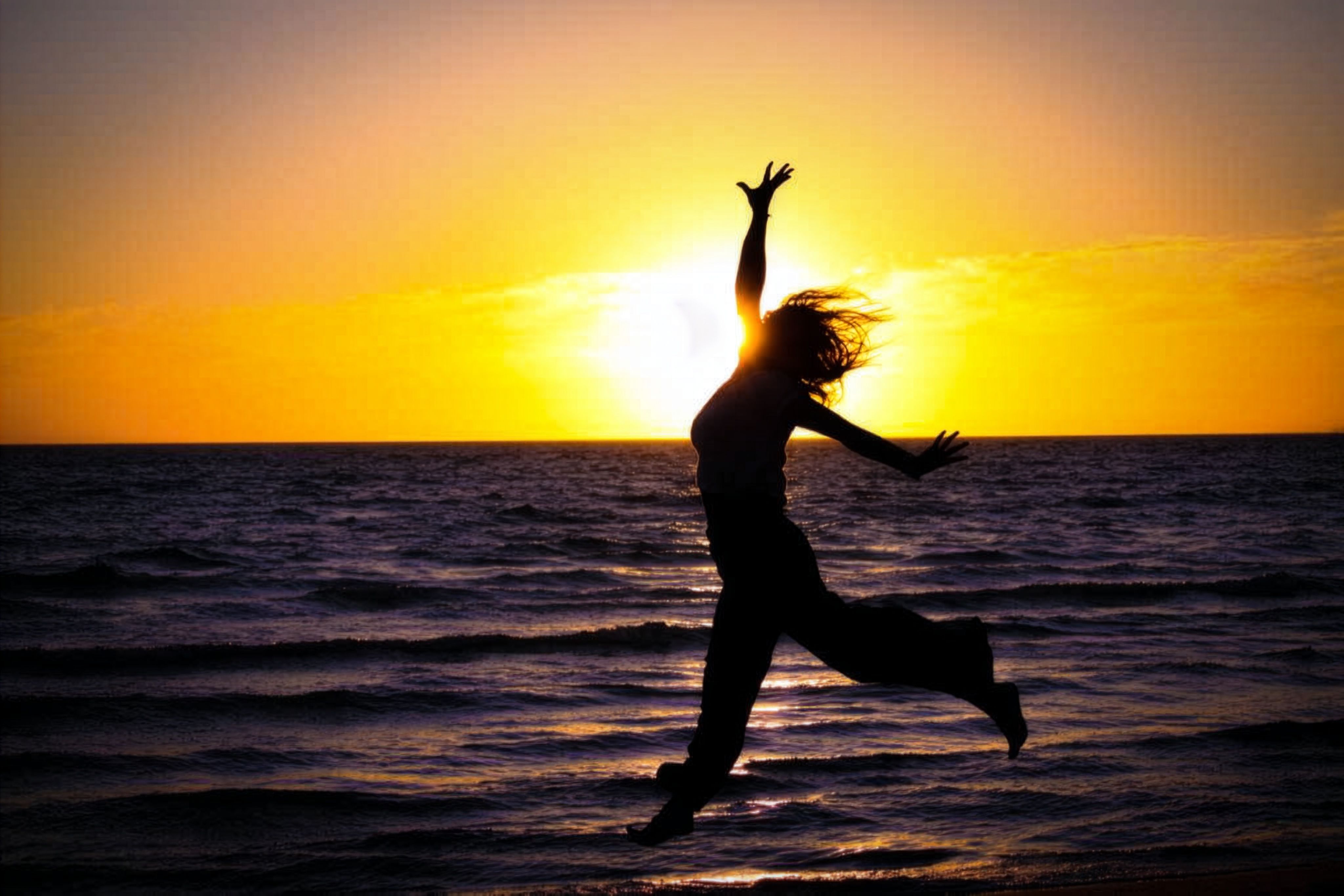 A person joyfully leaps on the beach at sunset, creating a beautiful silhouette.