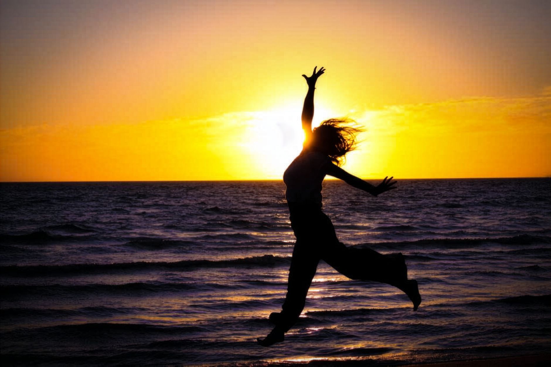 A person joyfully leaps on the beach at sunset, creating a beautiful silhouette.
