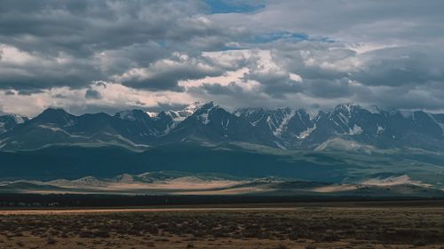 Free Scenic view of mountain range with cloudy sky casting shadows across the landscape. Stock Photo