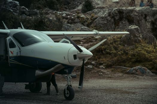 A small aircraft is parked in a rugged outdoor setting, showcasing its robust wings and propeller.