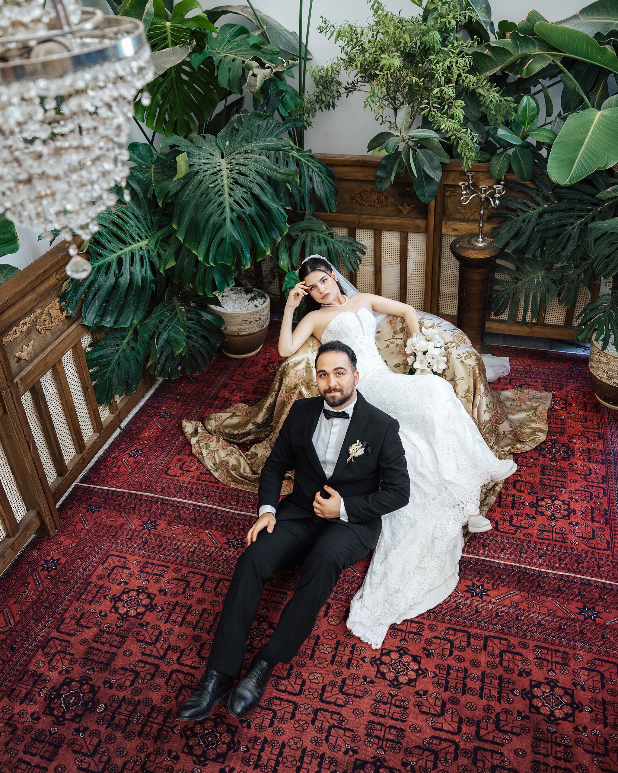 Bride and groom in elegant attire, surrounded by greenery in Antalya, Türkiye setting.