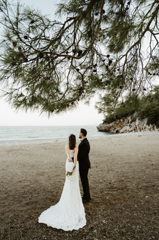 Bride and groom embrace on a serene beach in Antalya, Türkiye with a scenic view.