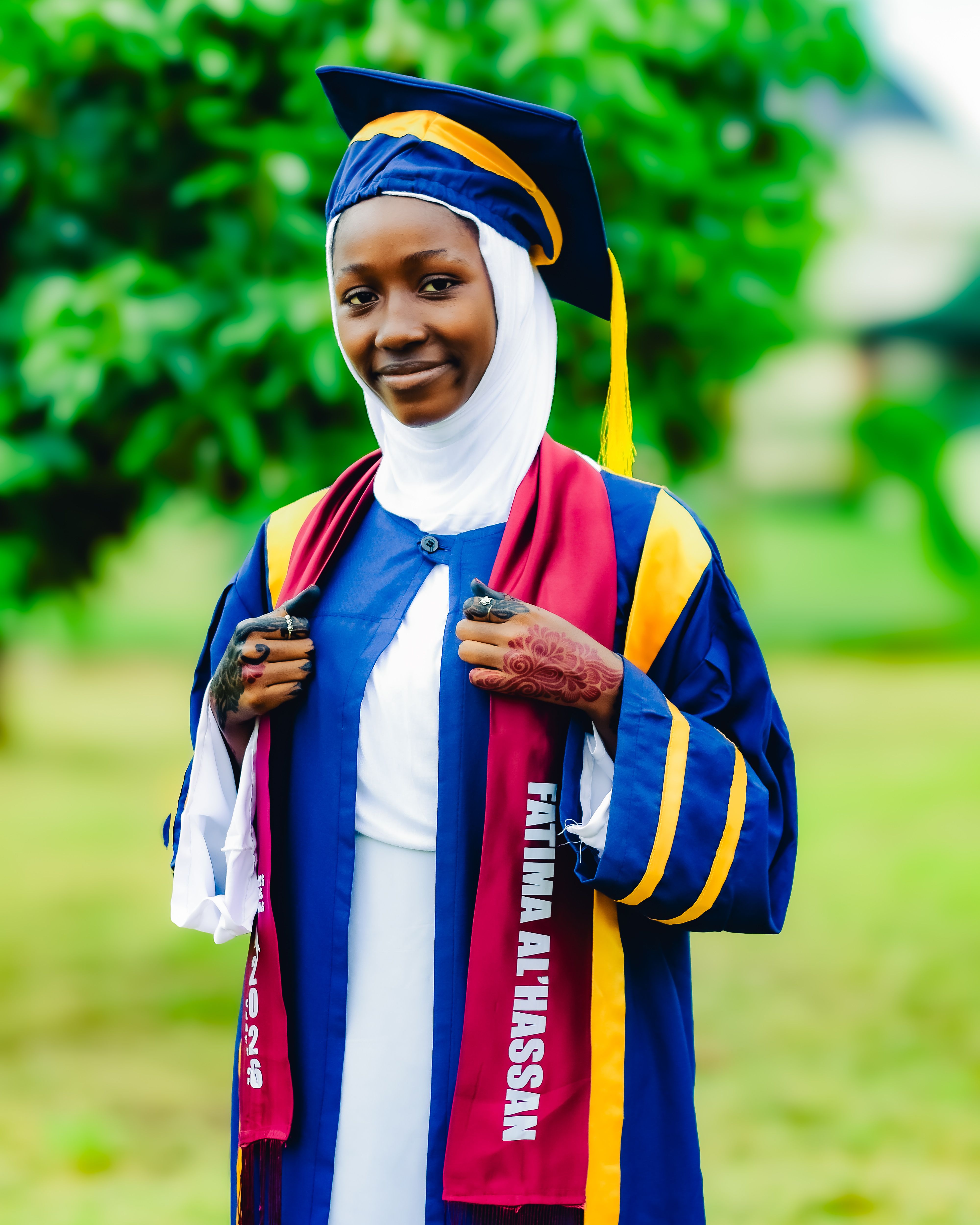 Young woman in graduation attire and hijab celebrates achievement outdoors in Abuja, Nigeria.