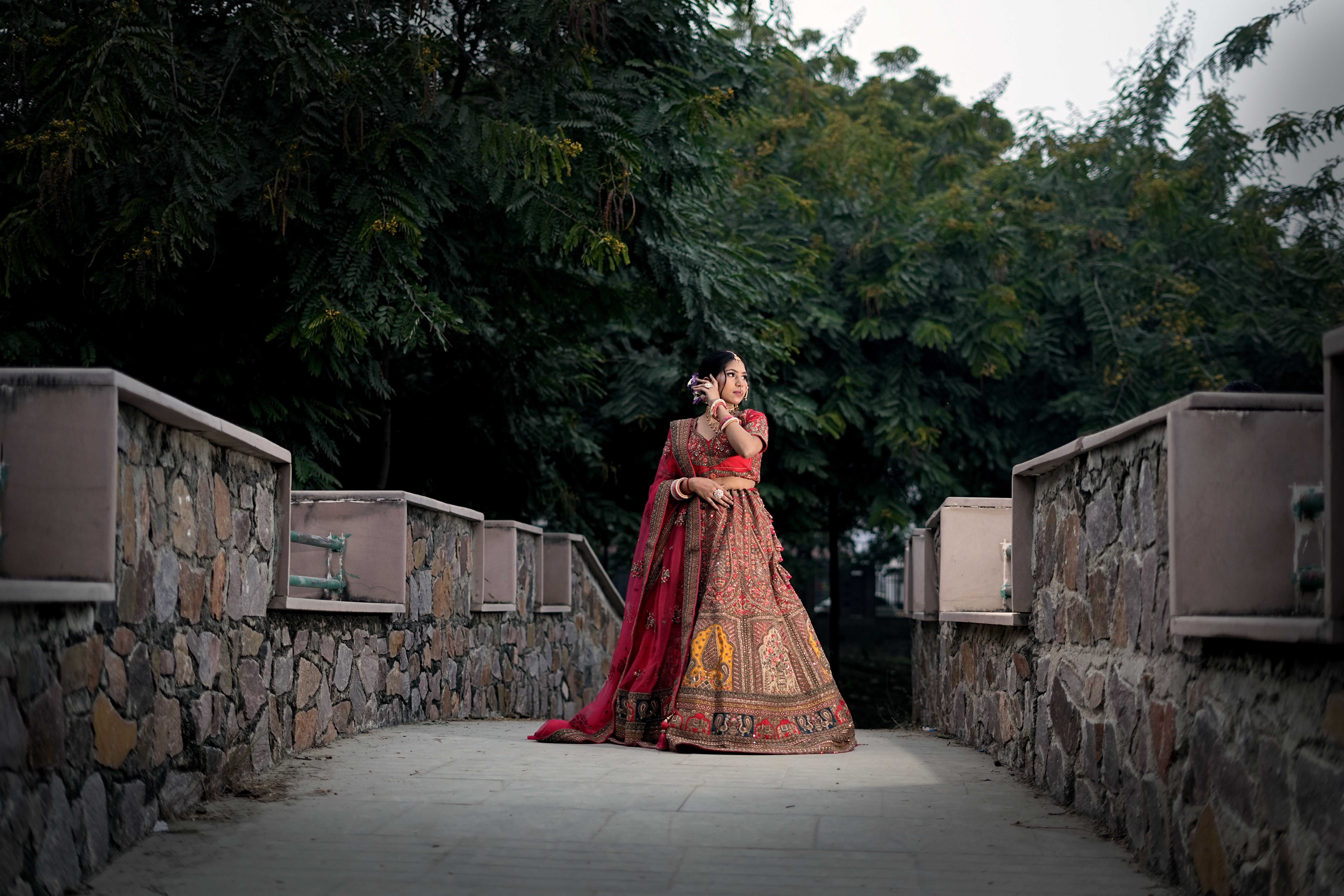 Beautiful Asian bride in traditional attire posing on a rustic stone bridge in Lucknow, India.