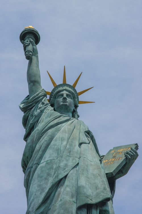 Free Iconic Statue of Liberty with torch and tablet set against a clear blue sky. Stock Photo