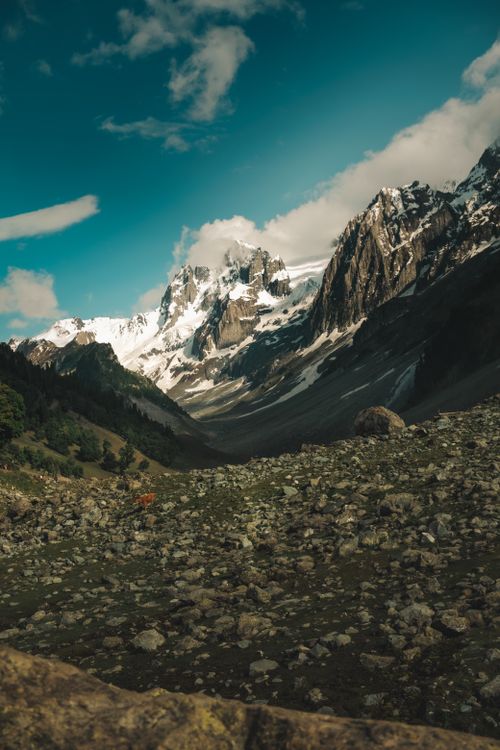 Free Stunning view of a rocky valley leading to towering snow-covered mountains under a bright blue sky. Stock Photo