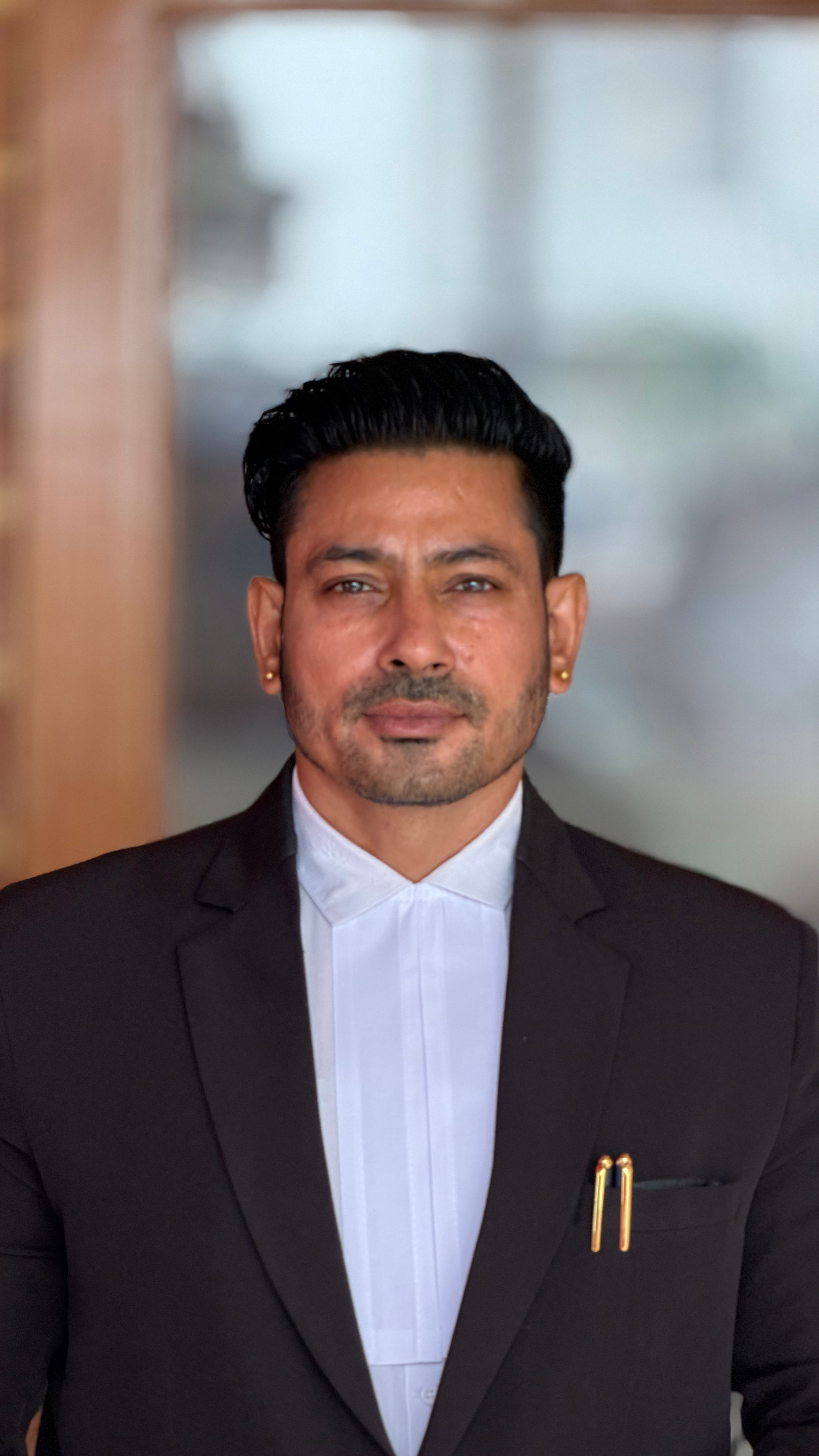 Confident businessman in a suit posing for a professional portrait indoors with a blurred background.