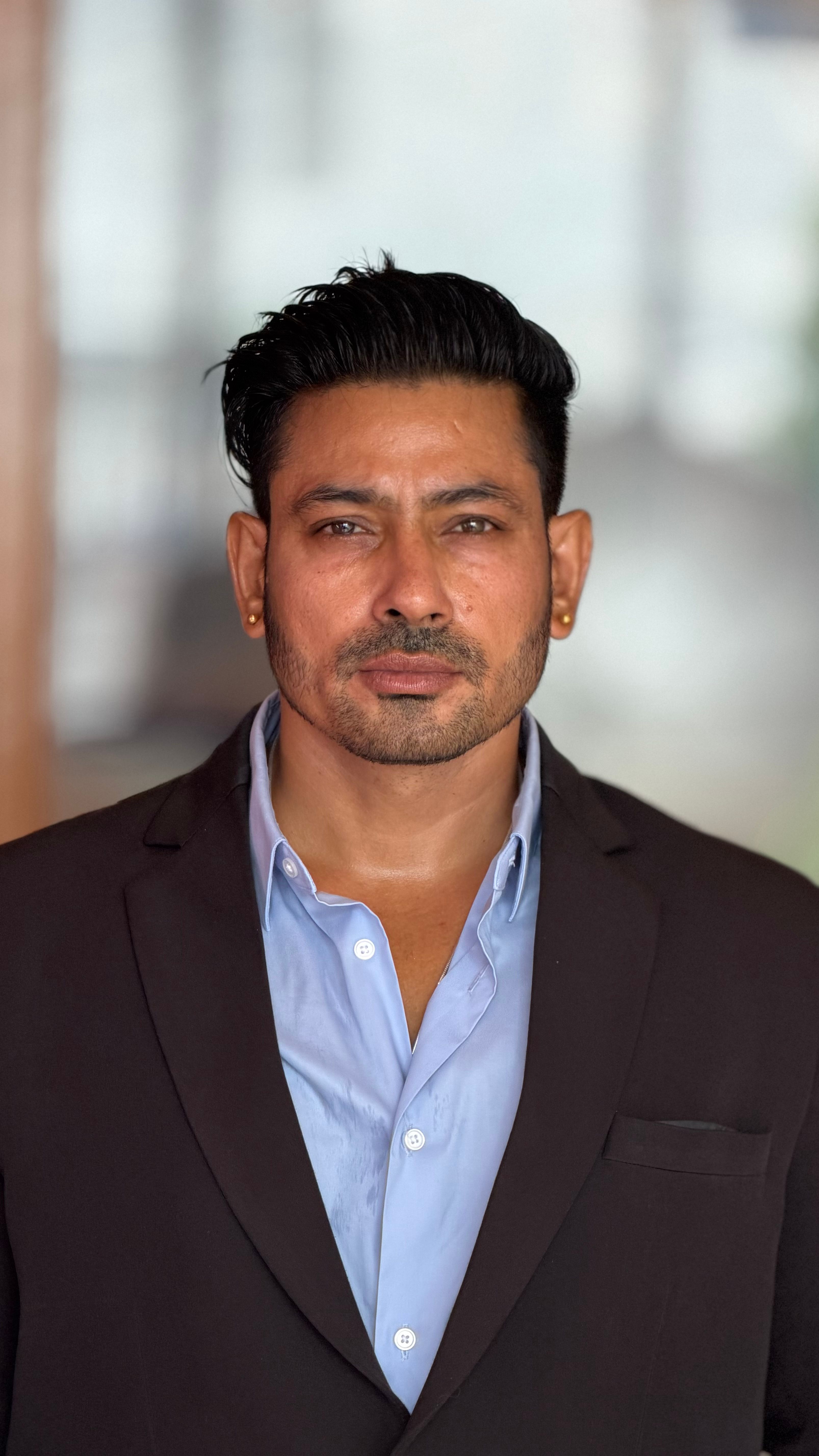 Portrait of a confident businessman wearing a black suit and blue shirt indoors.