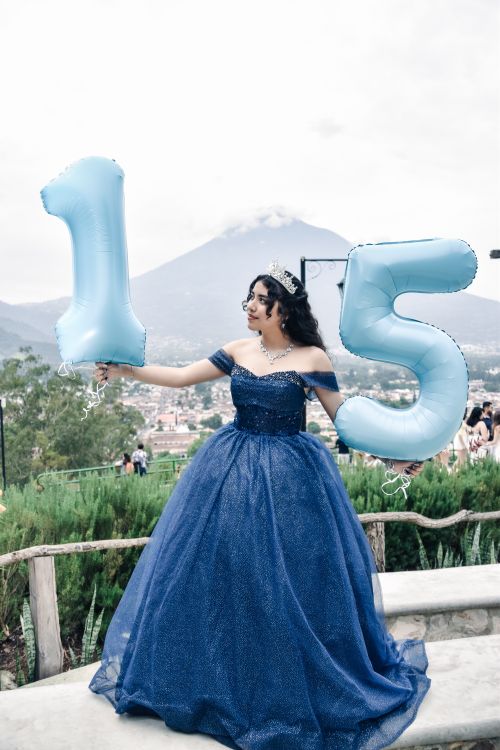 Free Young girl in blue gown celebrating quinceañera with balloons in front of a volcano. Stock Photo