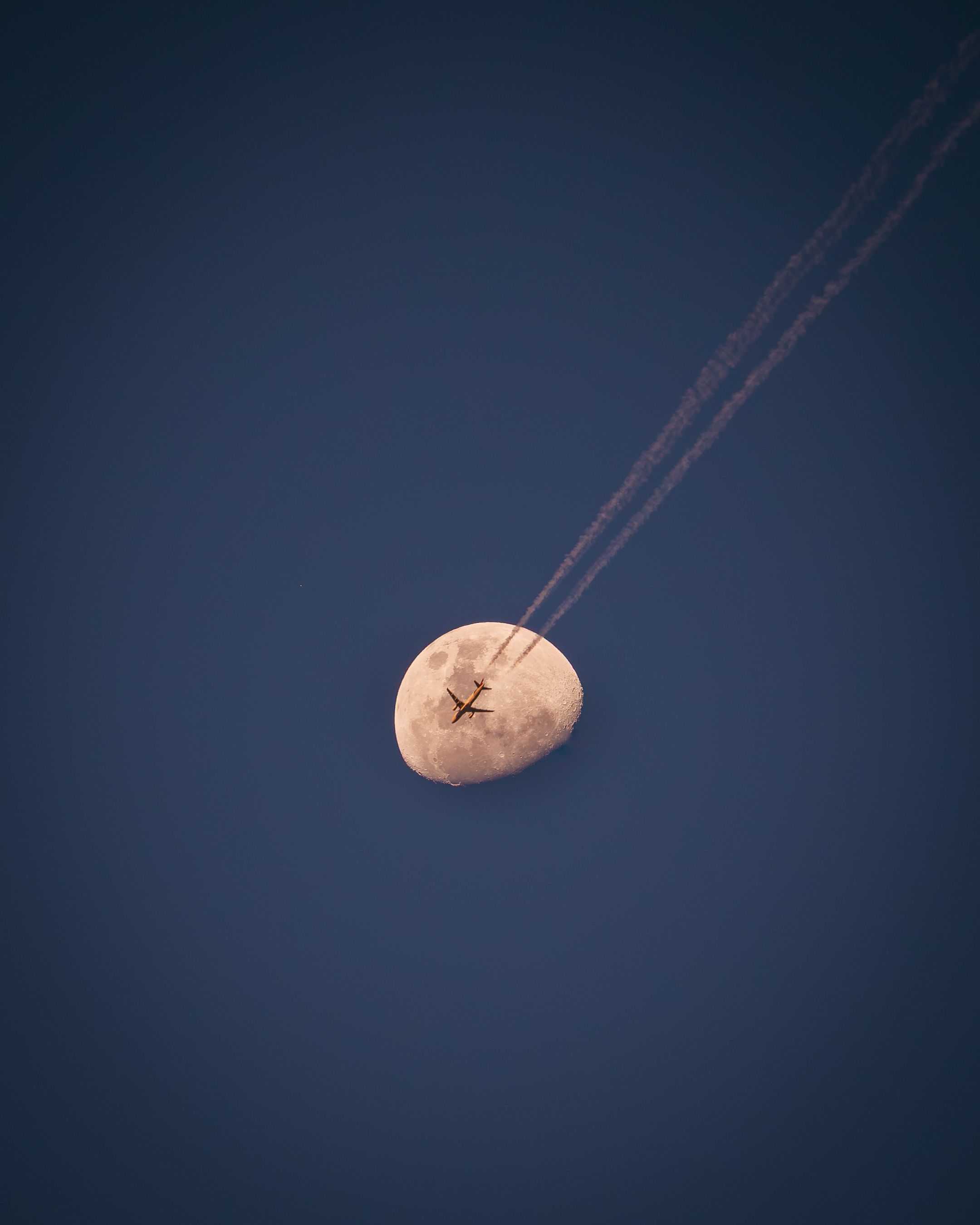 A striking capture of an airplane crossing in front of the moon against a clear, deep blue sky.