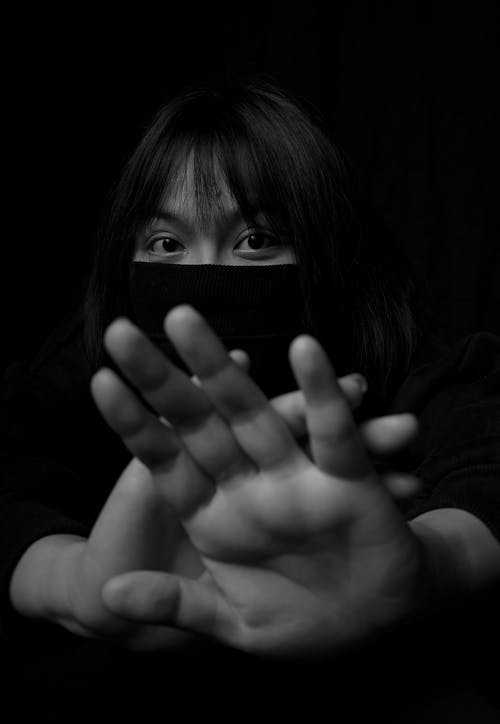 Young ethnic woman in black mask protecting with palms from approaching while maintaining social distance during coronavirus