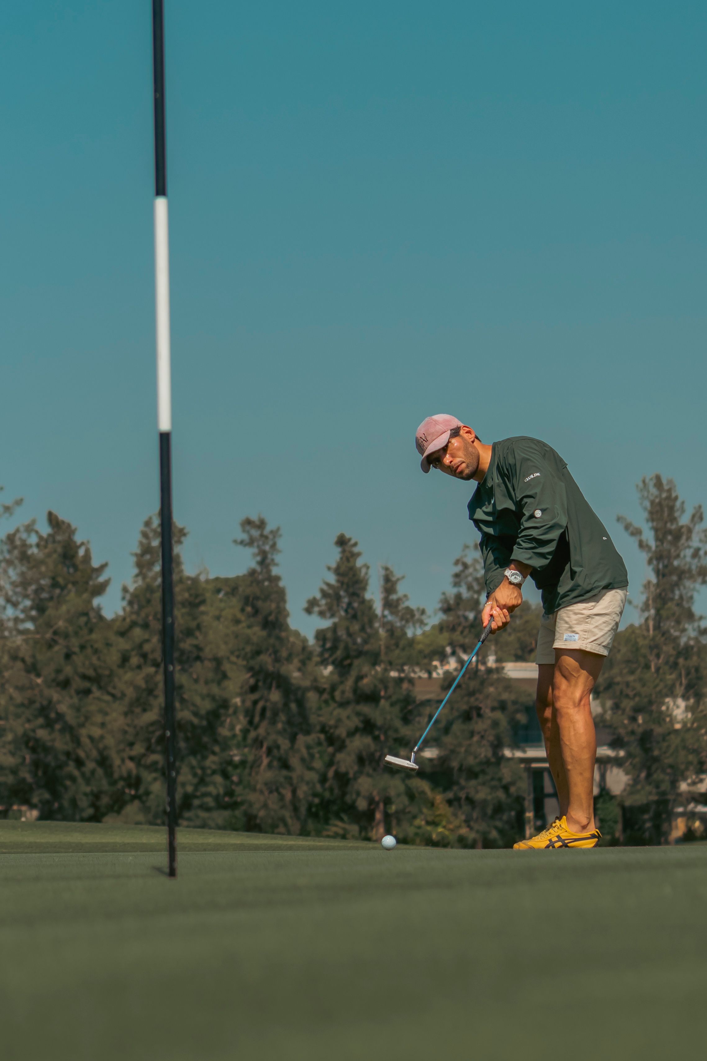 A man focuses while putting on a golf course under a clear sky, emphasizing concentration and leisure.