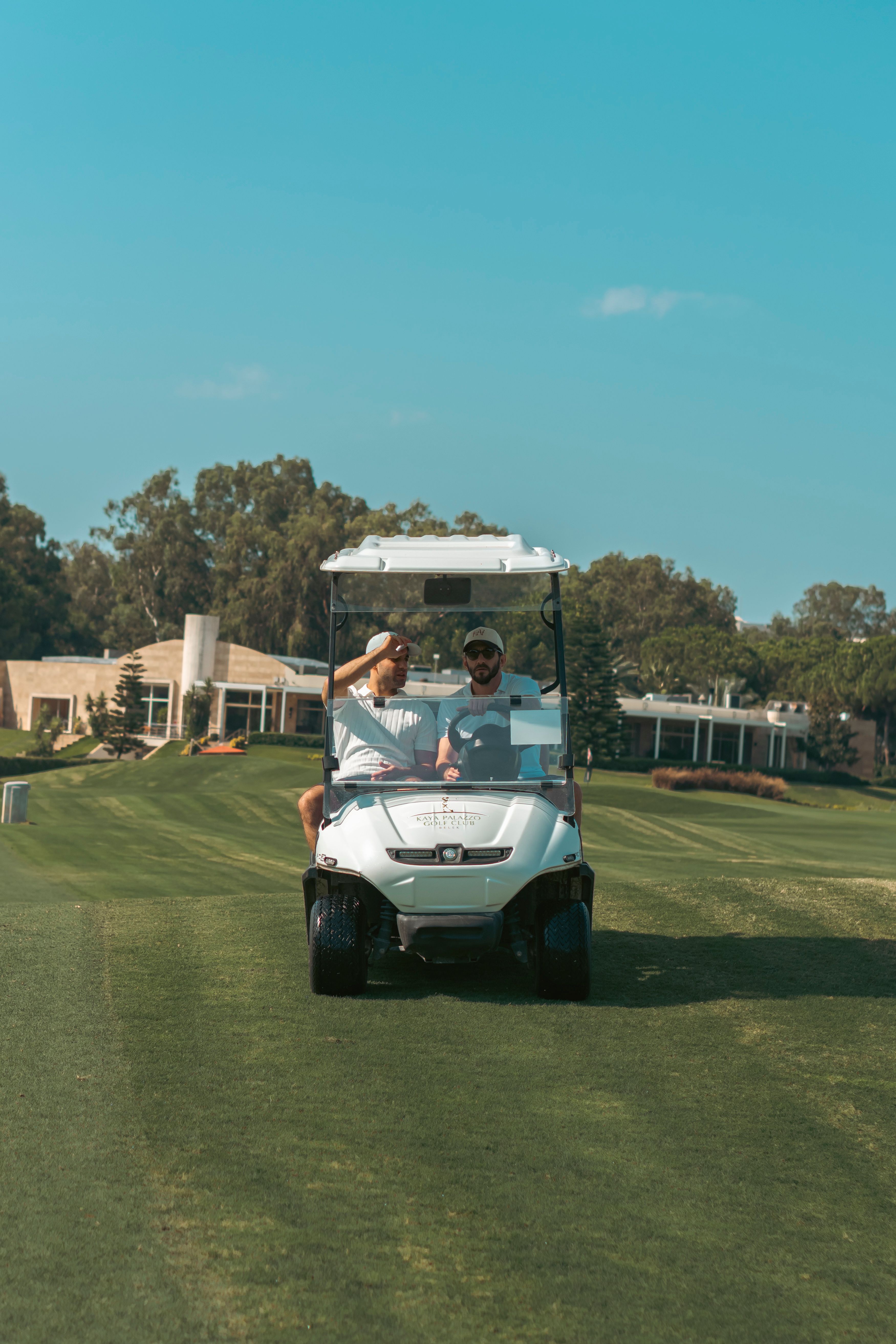 A couple riding a golf cart on a sunny day at a golf course, surrounded by lush greenery.