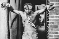 赤裸上身的男子穿着牛仔裤，靠在砖墙上摆出自信的姿势