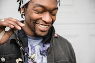 这是一张户外特写肖像，照片中一个留着辫子的男人闭着眼睛，面带微笑，显得十分快乐