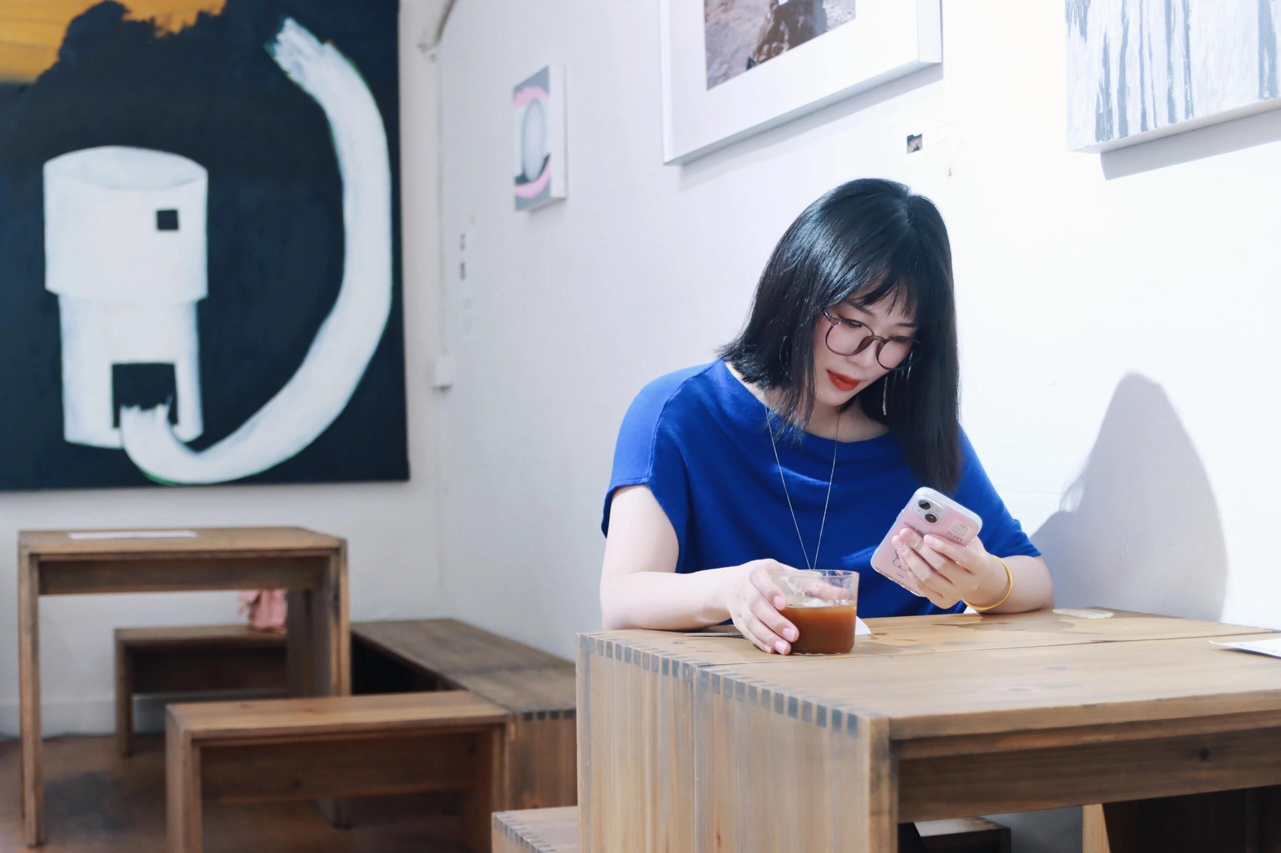 Woman in a cafe in Nanjing, China, using her smartphone while enjoying a drink. Interior setting with modern art.