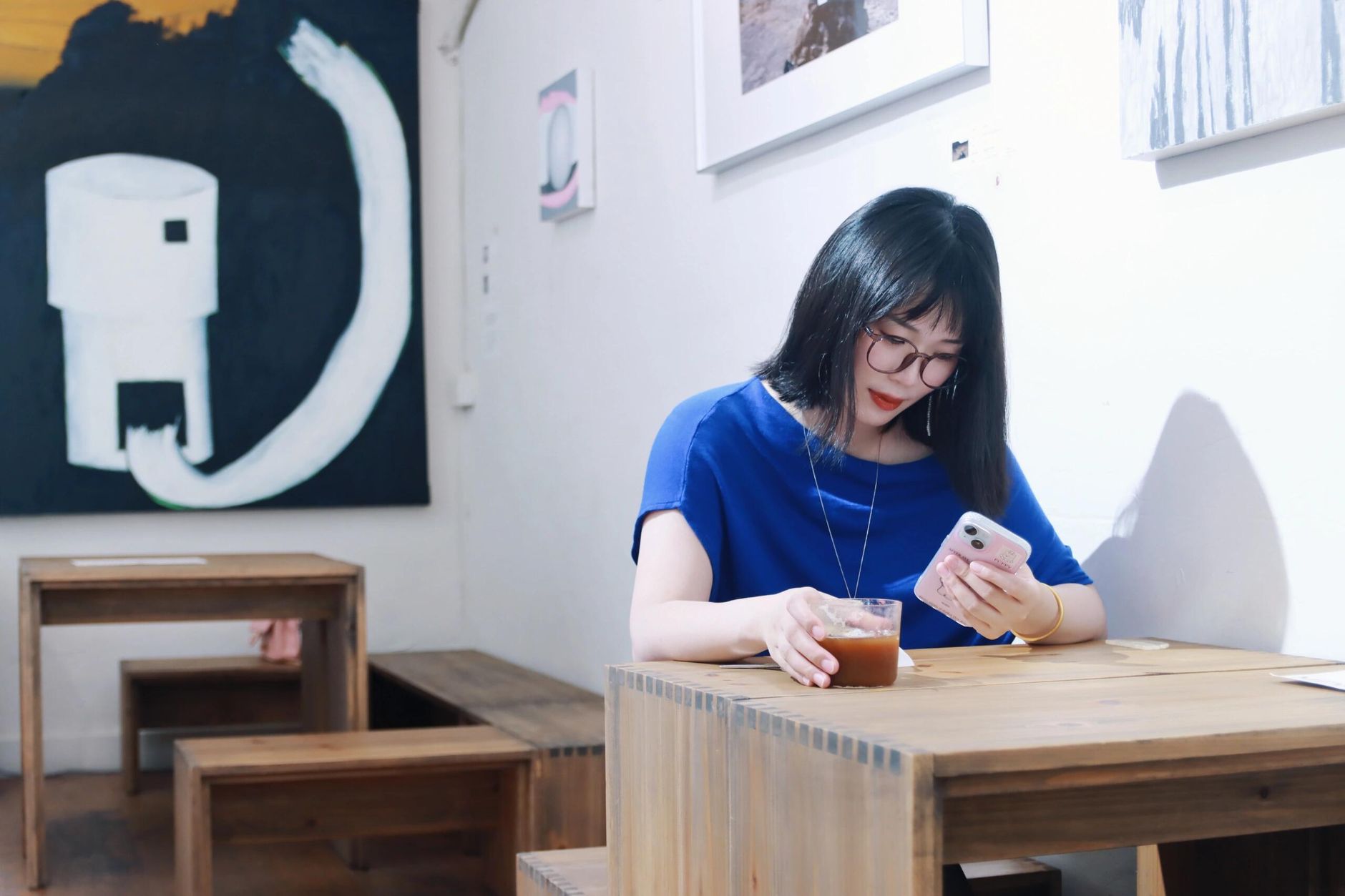 Woman in a cafe in Nanjing, China, using her smartphone while enjoying a drink. Interior setting with modern art.