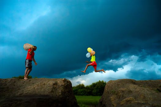 A child jumps with balloons between rocks under a stormy sky, creating a dramatic contrast.