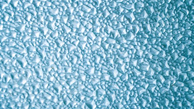 Close-up of a textured blue ice surface, revealing intricate patterns and details.