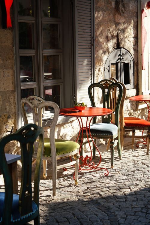Free Sunlit café with colorful chairs and tables on a cobblestone street in Izmir, Türkiye, capturing a warm morning vibe. Stock Photo