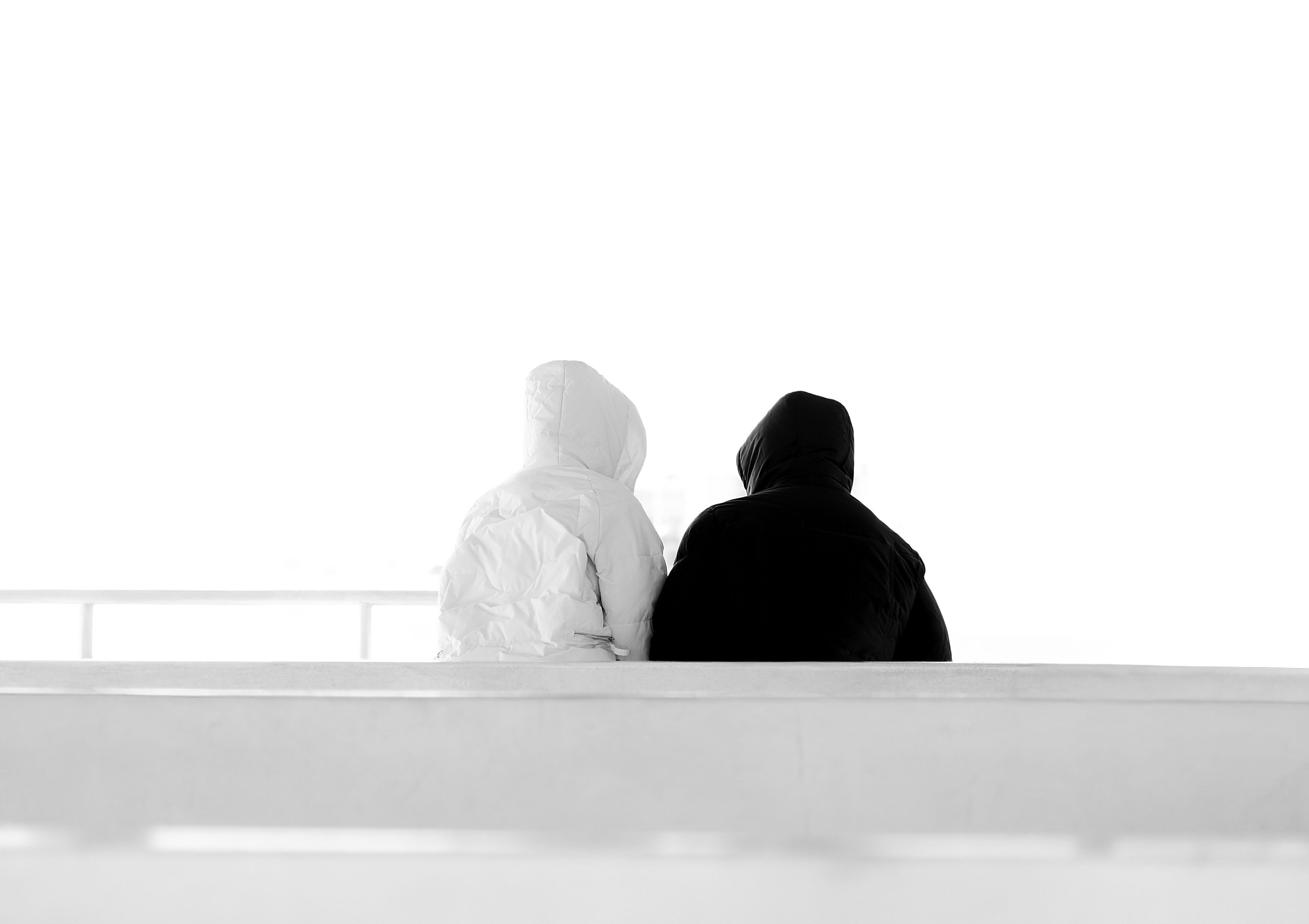 A minimalist, black and white photograph of two hooded figures sitting on a bench viewed from behind, in İstanbul.