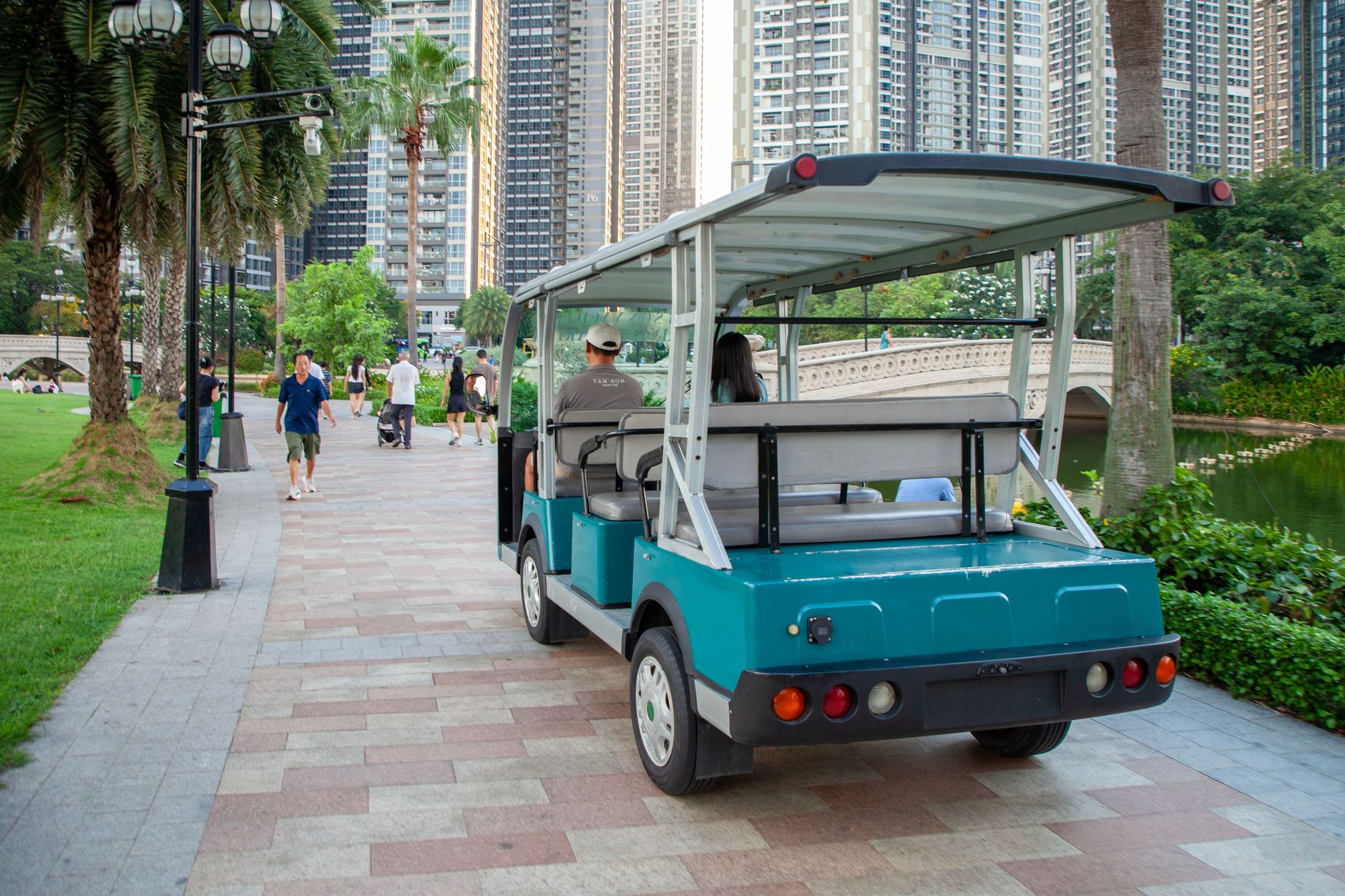 A golf cart on a park path with skyscrapers in the background on a sunny day.