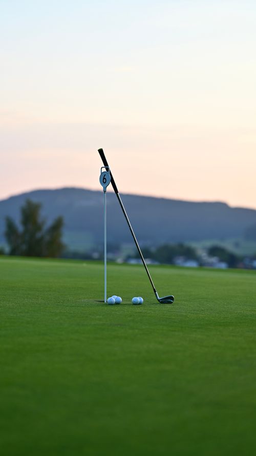 Free Close-up of golf club and balls near hole on serene golf course at sunset. Stock Photo