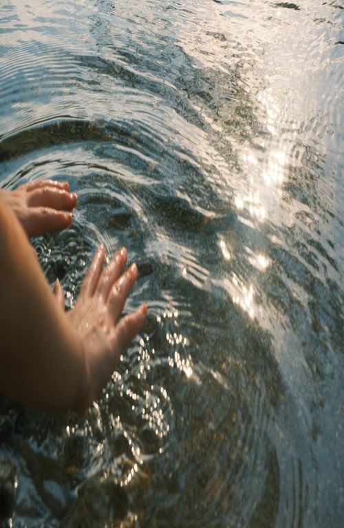 Free Close-up of hands touching water creating ripples under sunlight. Stock Photo
