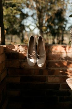 Chic white bridal shoes elegantly displayed on a rustic brick wall in natural light. - Fotografer Sidoarjo