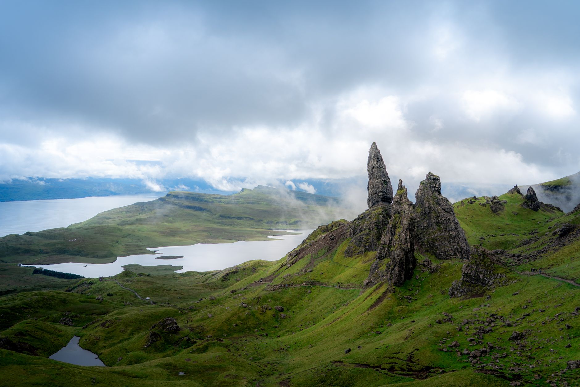 The jagged rock pinnacles of the Old Man of Storr rising from green slopes above a sea loch on the Isle of Skye, wreathed in cloud